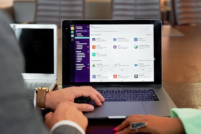 Two people working in Slack on a laptop